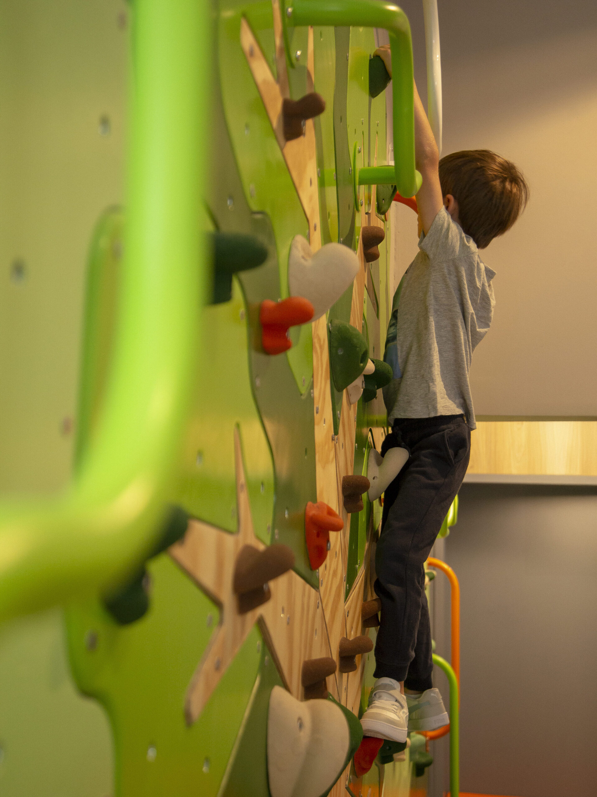 Criança escalando parede de brinquedoteca com escalada, desenvolvendo psicomotricidade